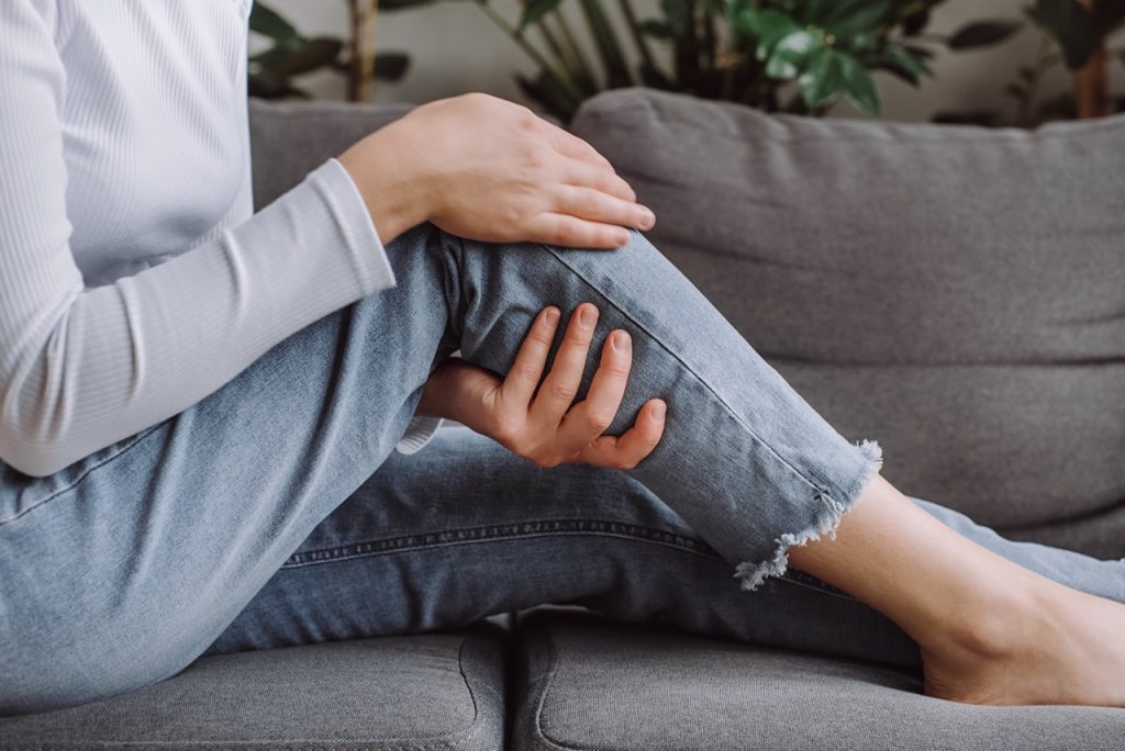 Person holding a painful joint suffering from knee osteoarthritis stiffness while sitting on a couch