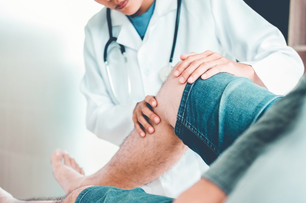 Doctor examining a patient's painful knee joint during a medical consultation for knee treatment