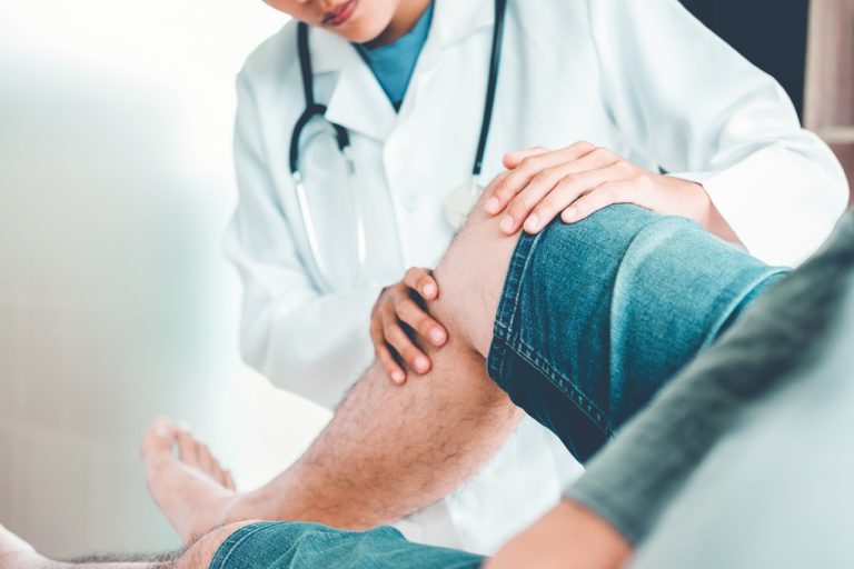 Doctor examining a patient's painful knee joint during a medical consultation for knee treatment