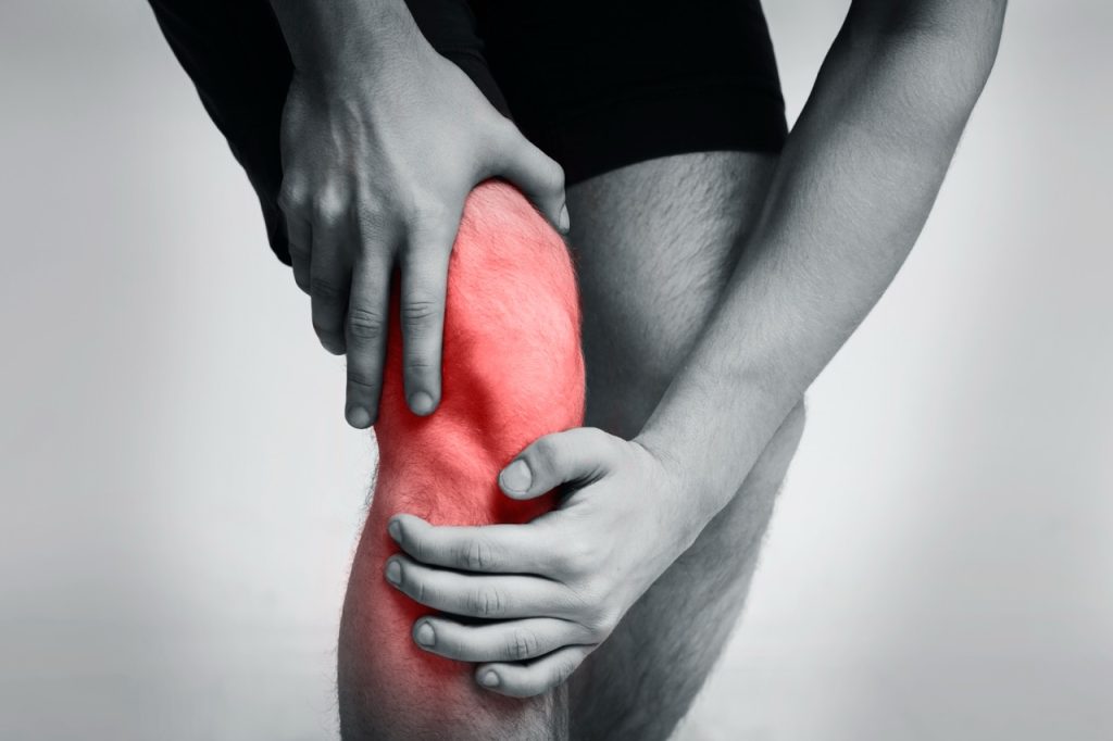 Close up of young sportsman feeling knee pain on jogging track.