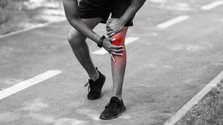 Close-up view of a runner holding a painful, inflamed knee on a running path.