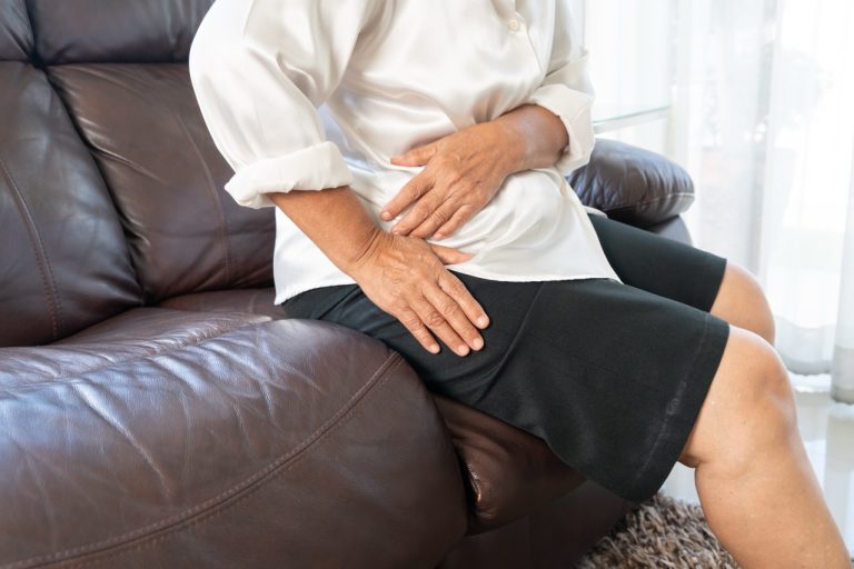 An older adult holding their sore knee while sitting down, showing how knee pain can affect your hips and body alignment.