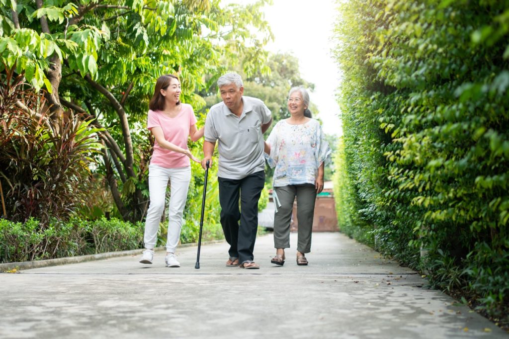 Elderly man walking in a garden using a cane due to an unsteady knee and joint pain.