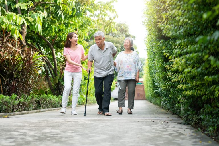 Elderly man walking in a garden using a cane due to an unsteady knee and joint pain.