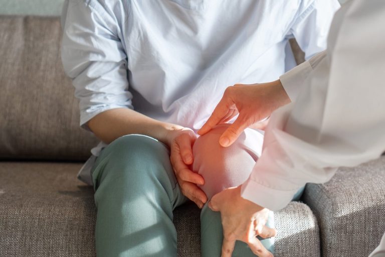 Doctor examining a patient's swollen joint suffering from chronic knee pain during a medical evaluation