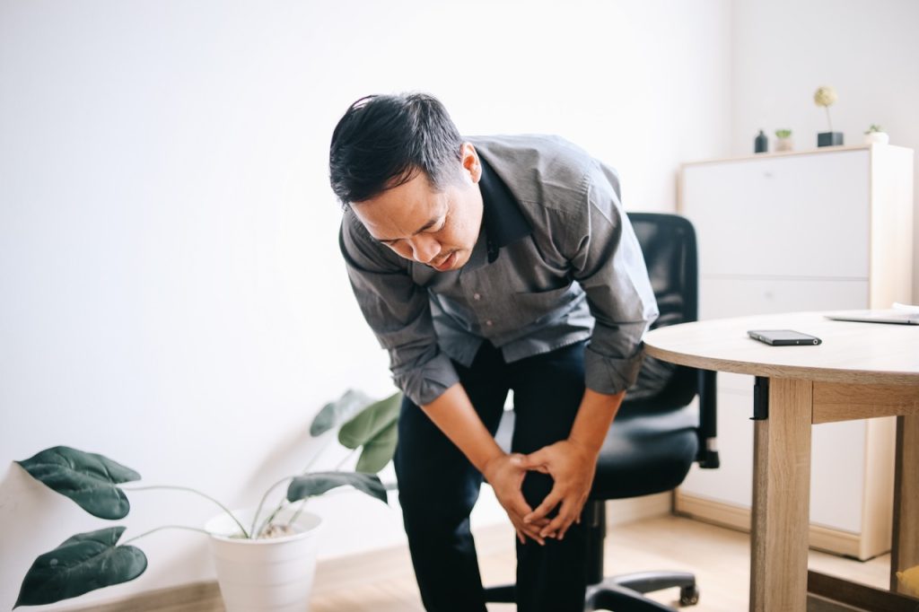 Man holding his knee in discomfort while sitting at a desk due to knee pain at work.