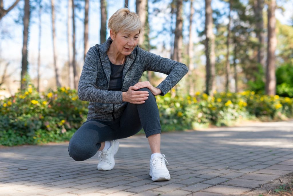 Close up of young sportsman feeling knee pain on jogging track.