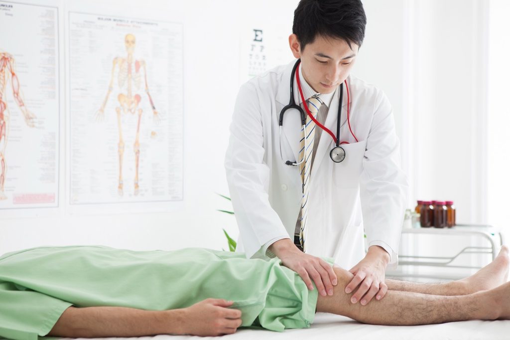 Doctor examining a patient's painful, weak knee during a medical consultation