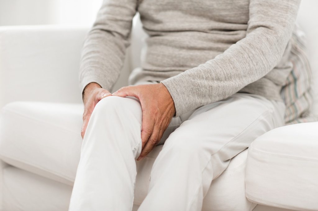 Older man holding his painful, swollen knee while sitting down