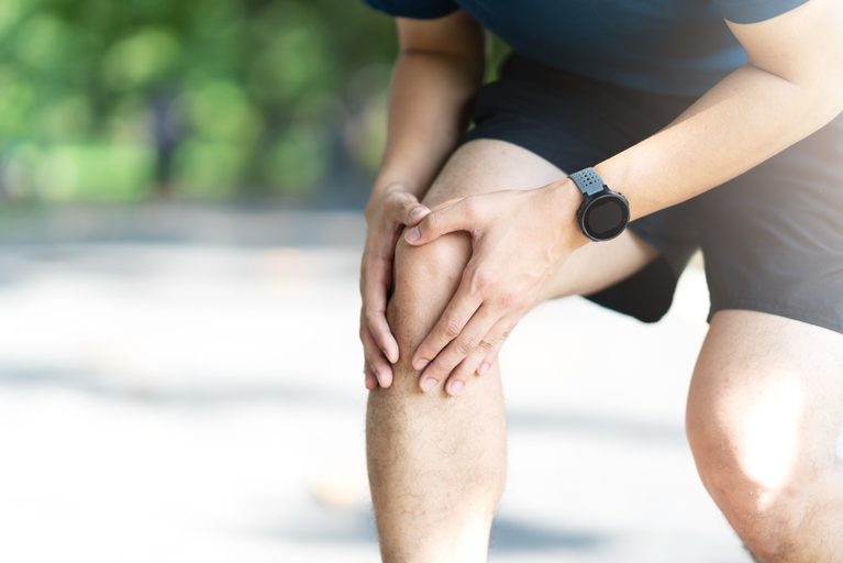 Young athletic man holding his painful knee while resting during a outdoor run