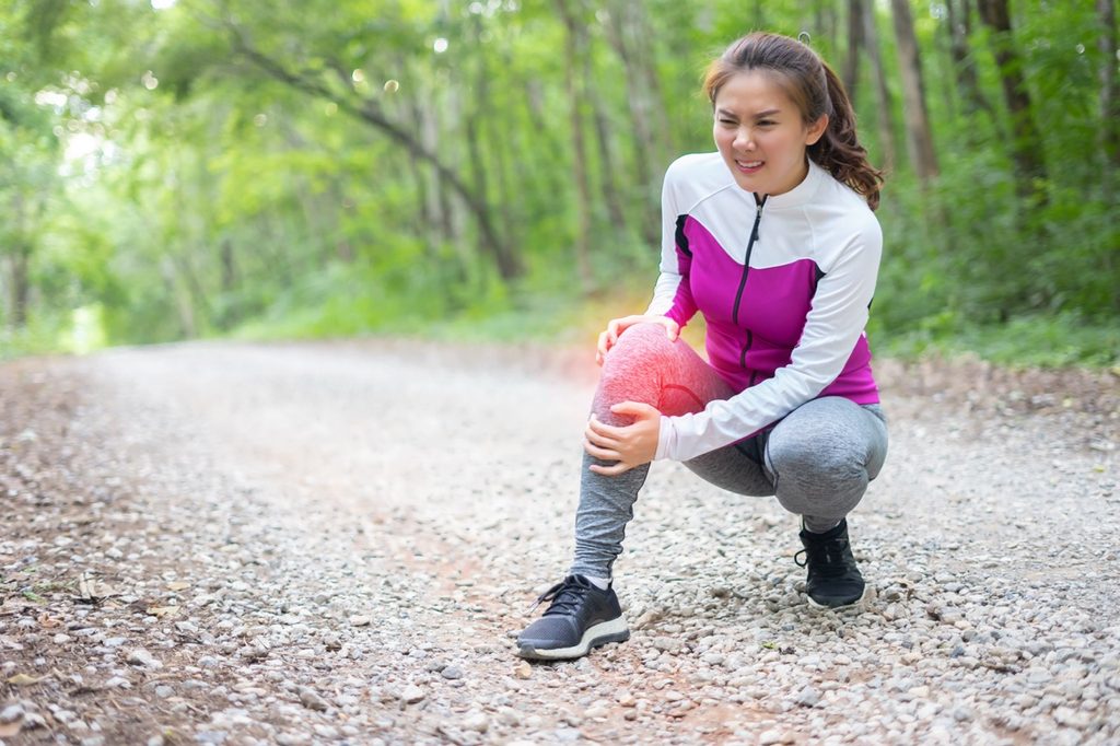 Young Asian runner crouching on a path while holding her painful knee