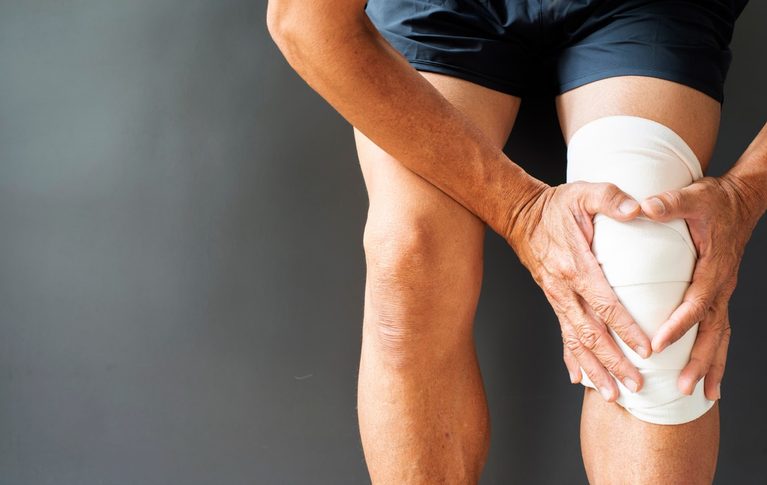 Older person holding their painful knee while seated indoors