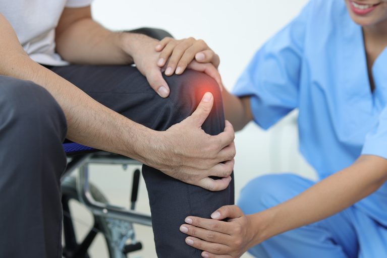 Medical professional examining a patient's painful, swollen knee during a consultation