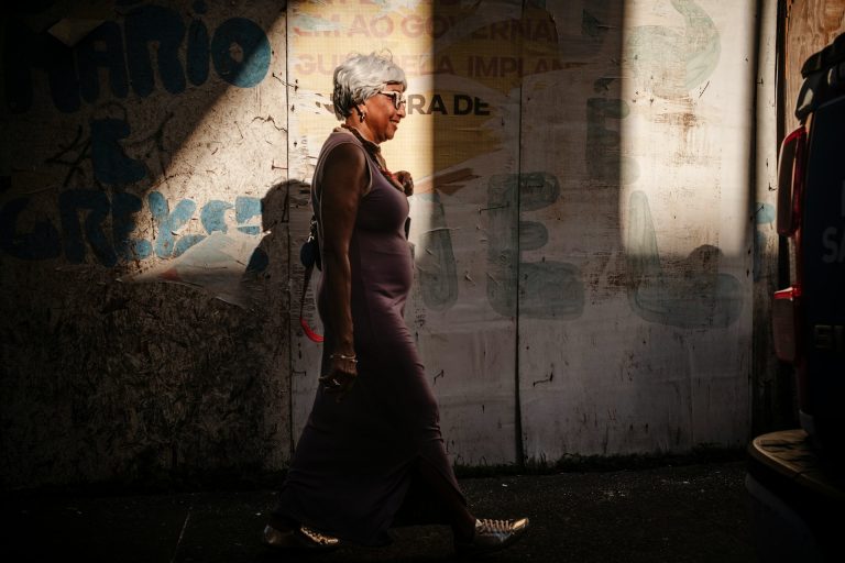 Older woman walking at a steady pace along a sunlit city sidewalk, staying active with knee arthritis